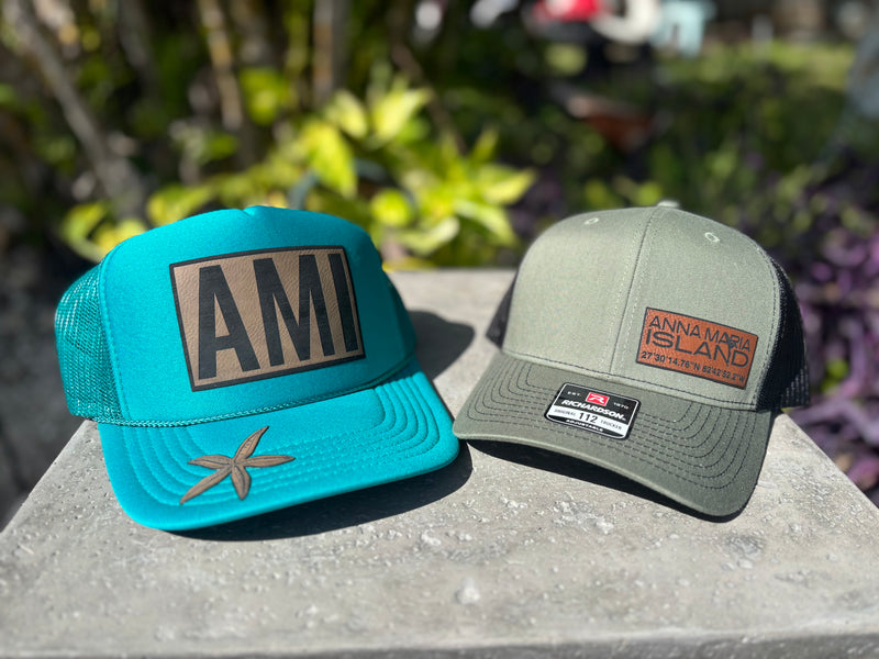 A blue hat and a dark green hat with leather patches laser engraved by Gnarly Mangrove Designs.